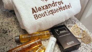 Una encimera de baño con artículos de aseo, una toalla blanca y una caja negra con la etiqueta 'Alexandros Boutique Hotel'.