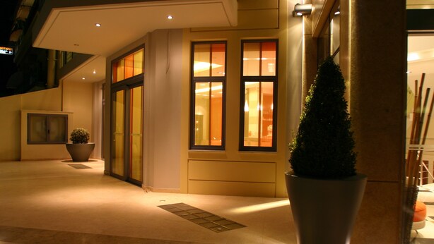 A hotel entrance with a tiled floor, a potted plant, and a large window with warm interior lighting. - Alexandros Boutique Hotel (Argos-Mykines)
