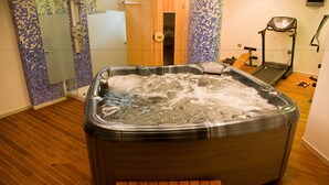 A hot tub in a room with wooden flooring, a treadmill, and a shower area with mosaic tiles. - Alexandros Boutique Hotel (Argos-Mykines)