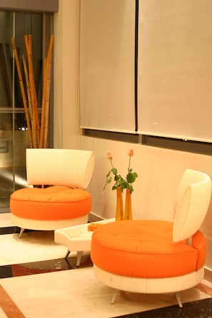 Una habitación moderna con dos sillas naranja y blanco, una mesita y un florero con flores.
