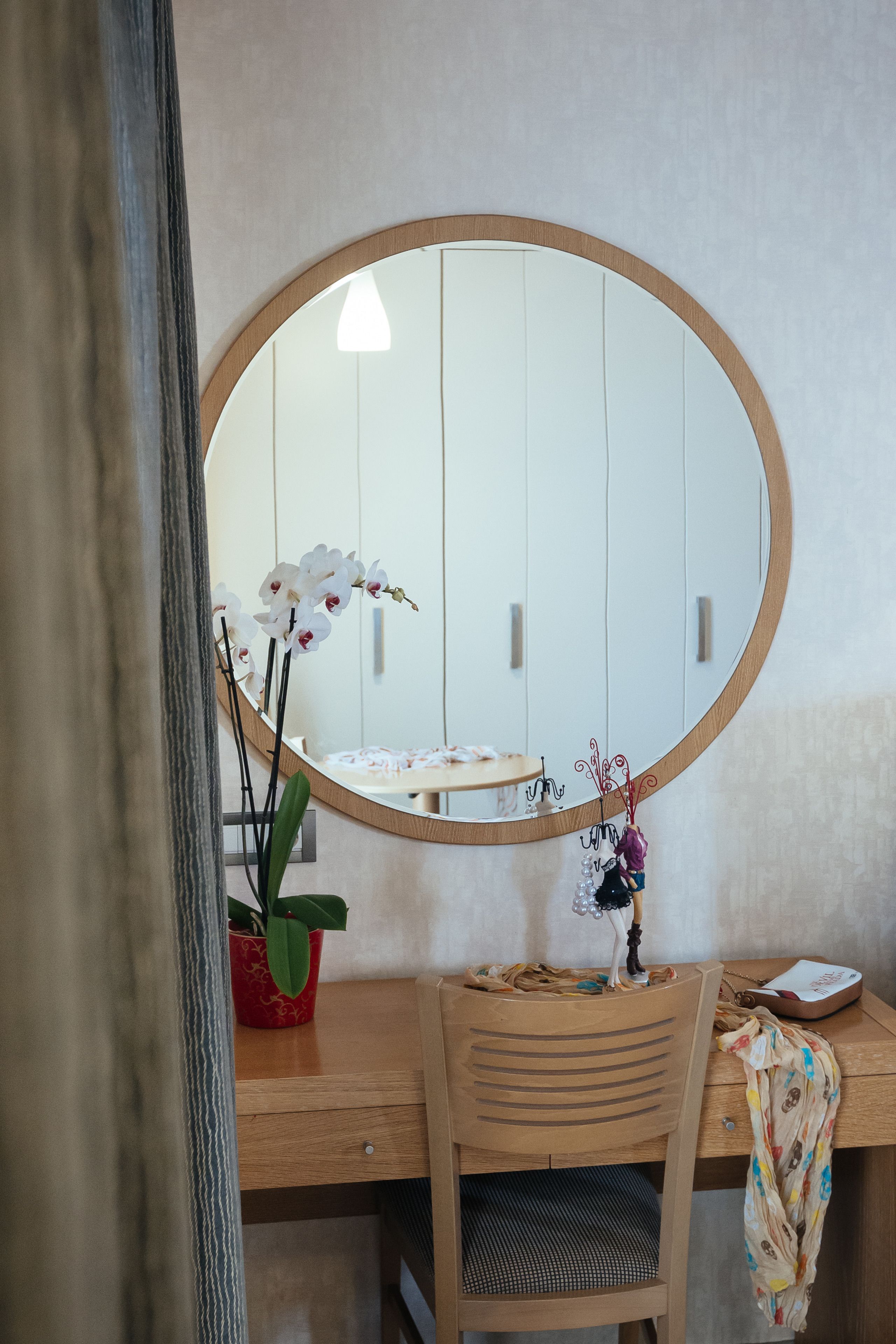 Een houten bureau met een ronde spiegel, een stoel, een potplant en een klein tafeltje met een decoratief object.