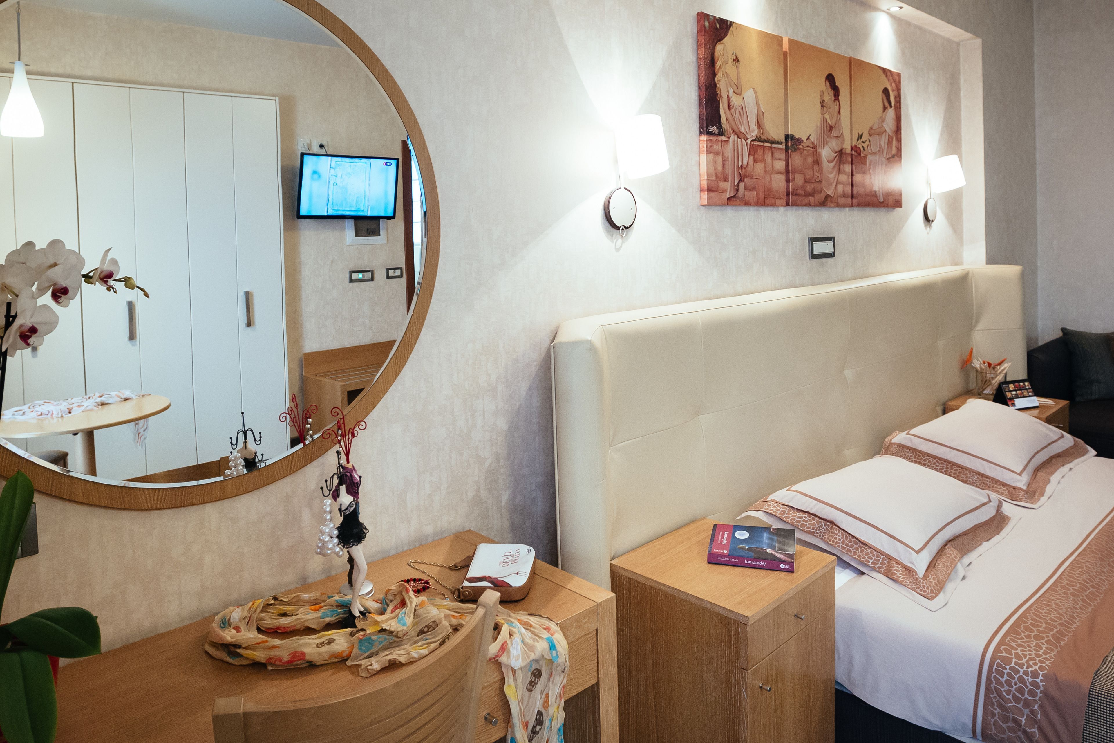 A hotel room with a large bed, a bedside table with a lamp, a TV on the wall, and a painting above the bed.