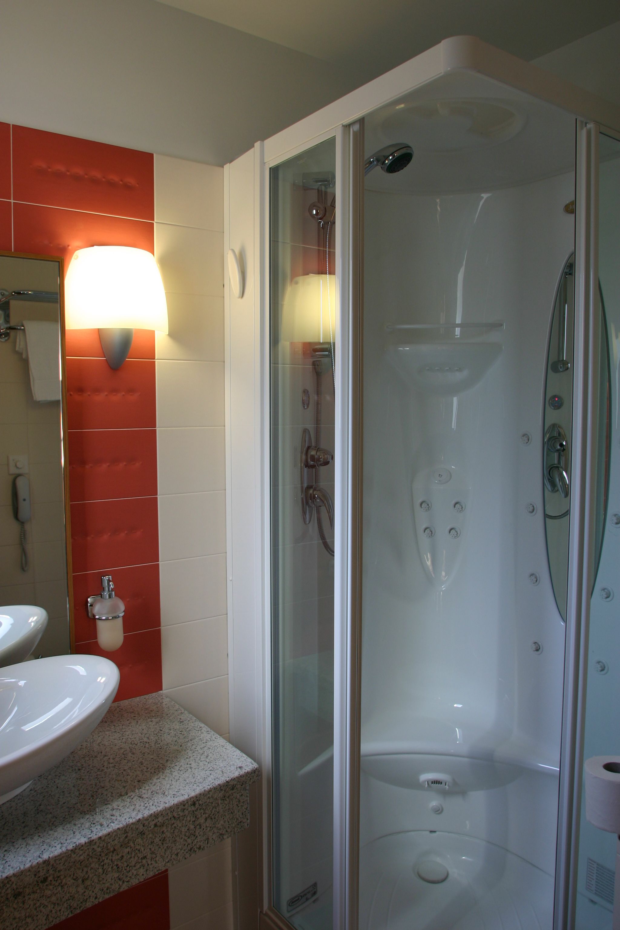 Een moderne badkamer met een douchecabine van glas, een wastafel en een spiegel met een inbouwlamp.