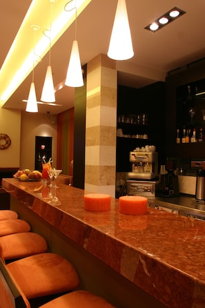 Zona de bar con encimera de mármol, lámparas colgantes y una máquina de café.
