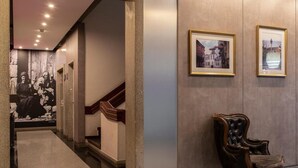 A hallway with a staircase, framed pictures on the wall, and a leather armchair. - Samasa Fundão (Fundao)