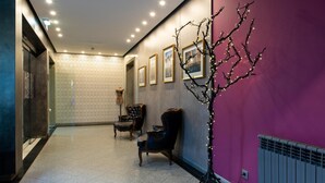 A hallway with a tiled floor, a purple wall, and a decorative tree with lights. There are framed pictures on the wall and two upholstered chairs. - Samasa Fundão (Fundao)