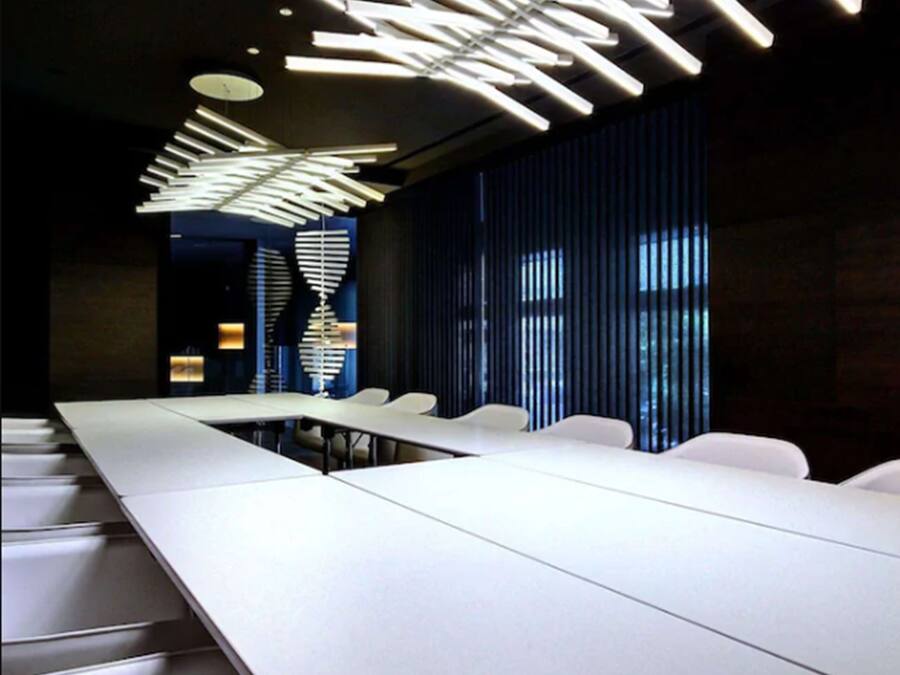 Une salle de conférence avec une longue table, des chaises et un luminaire moderne au plafond.