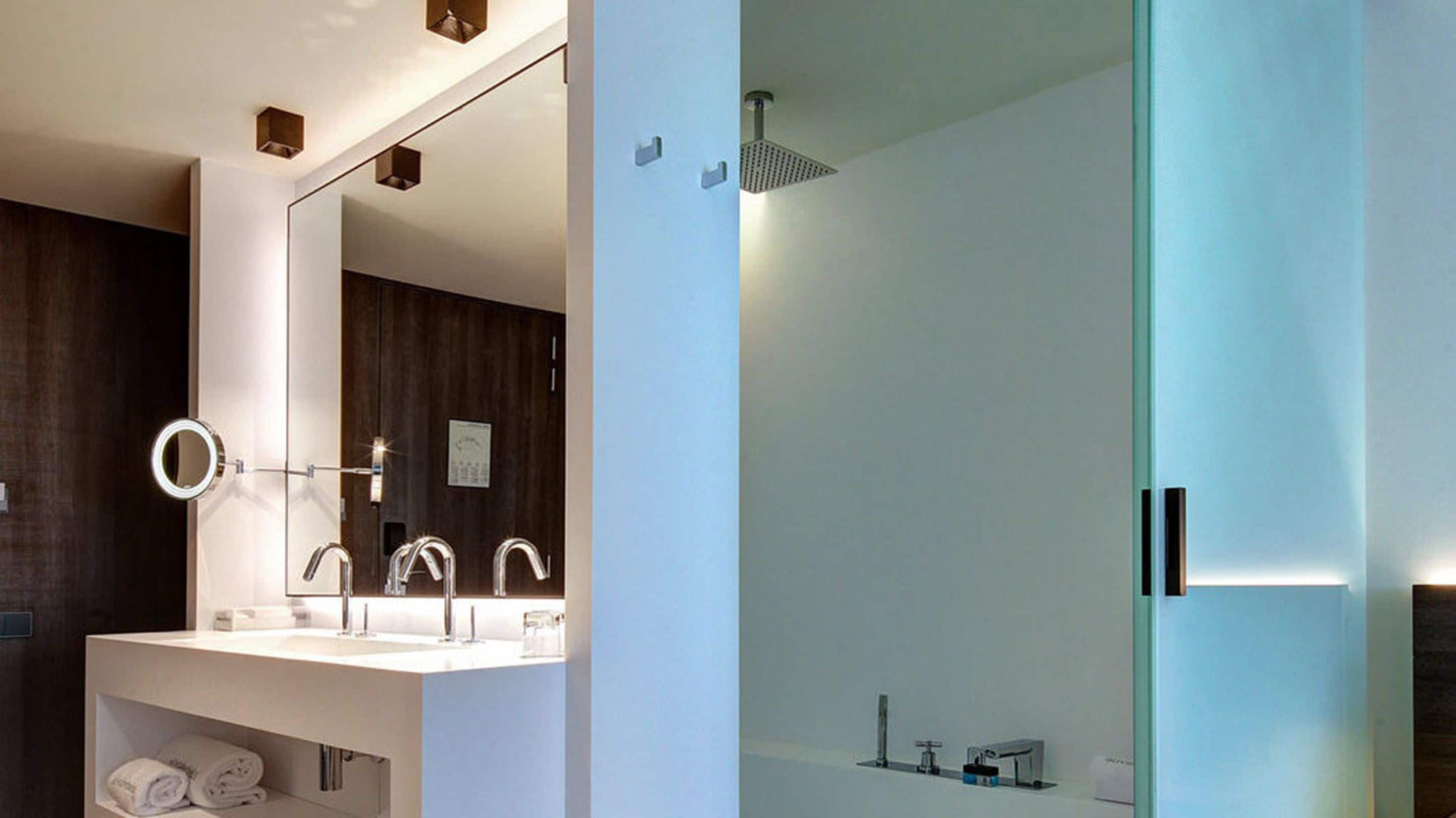 Un baño moderno con un espejo grande, tres lavamanos y una ducha.