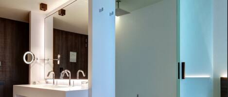 A modern bathroom with a large mirror, a built-in sink, and a glass-enclosed shower.