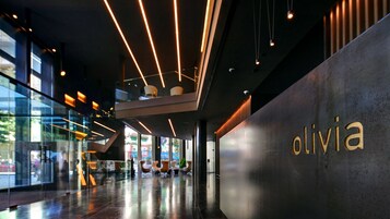 Um lobby moderno com fachada de vidro, escadaria central e um letreiro chamativo 'olivia' na parede.