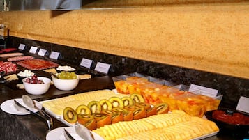 Un bufé con diversos alimentos, entre ellos frutas cortadas, quesos y postres.