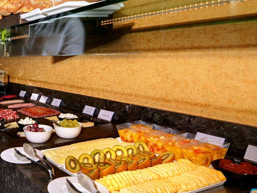 Un bufé con diversos alimentos, entre ellos frutas cortadas, quesos y postres.
