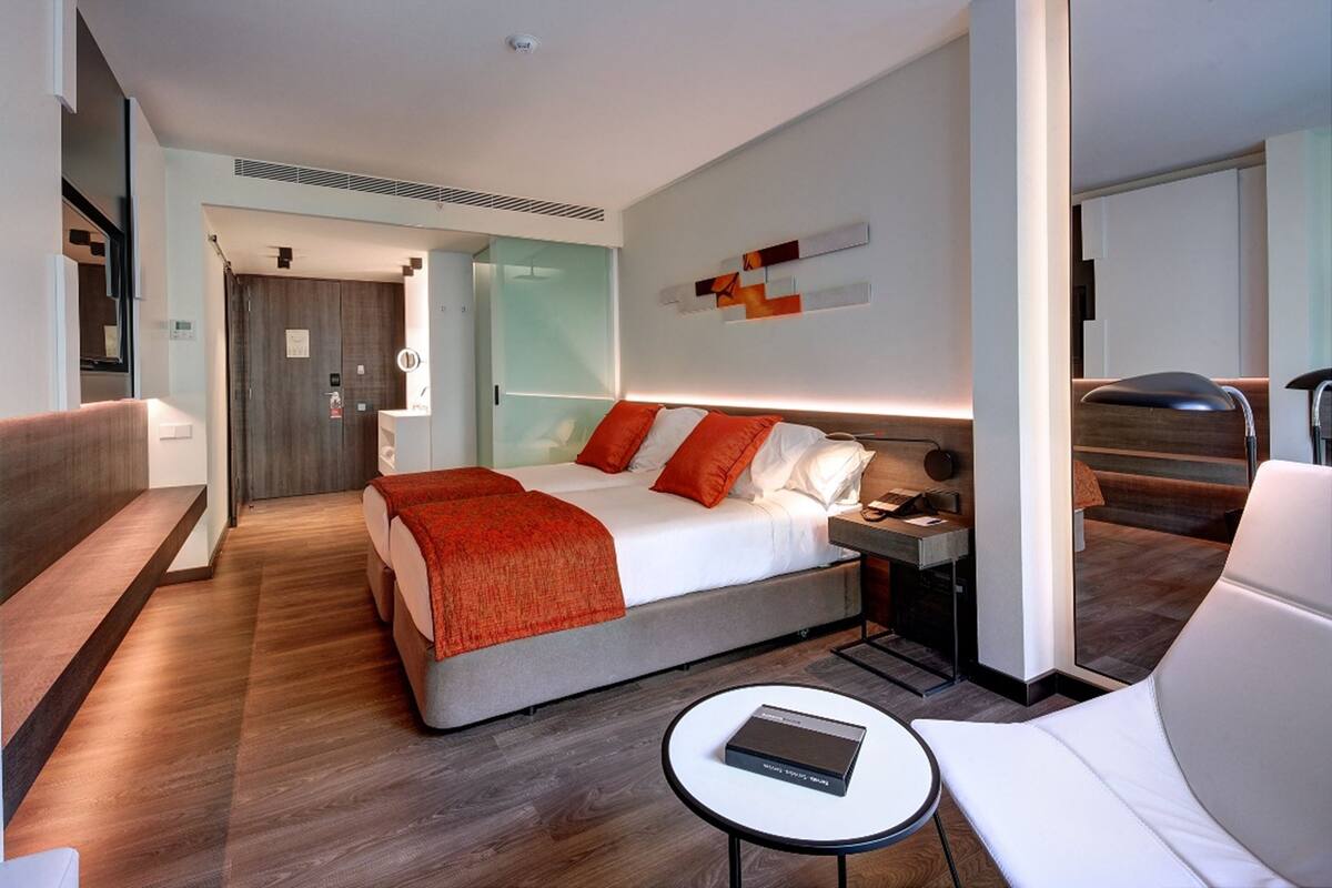 A modern hotel room with a large bed, a bedside table, a chair, and a small table.