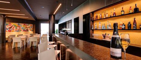 A modern bar area with a long counter, white chairs, and a variety of liquor bottles.