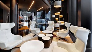A modern lobby with white leather sofas, round tables, and a staircase in the background.