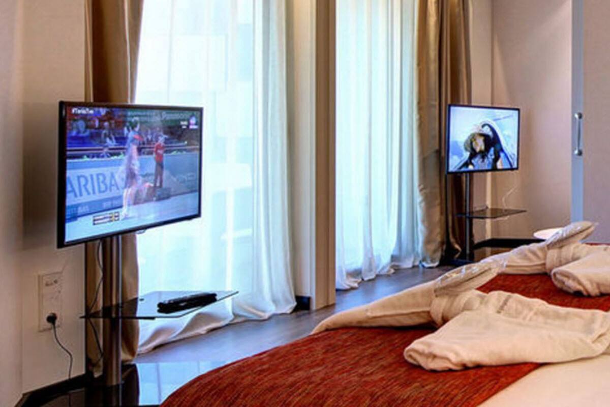 A hotel room with a bed, two televisions, a red throw blanket, and a red pillow.