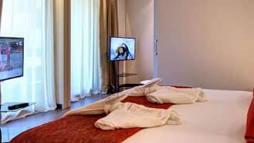 A hotel room with a bed, two televisions, a red throw blanket, and a red pillow.