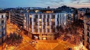 A modern hotel with a corner location, featuring a glass facade, multiple floors, and a rooftop terrace.