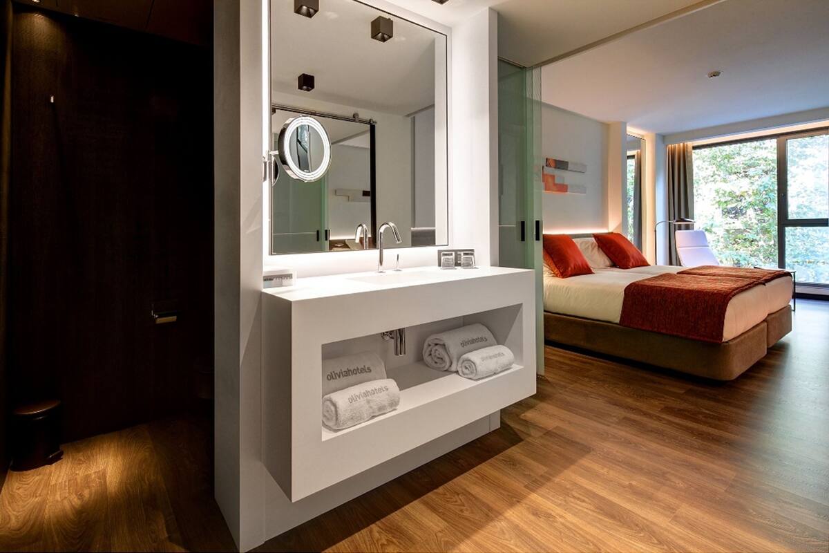 A modern hotel room with a large mirror, a bed with red pillows, and a wooden floor.