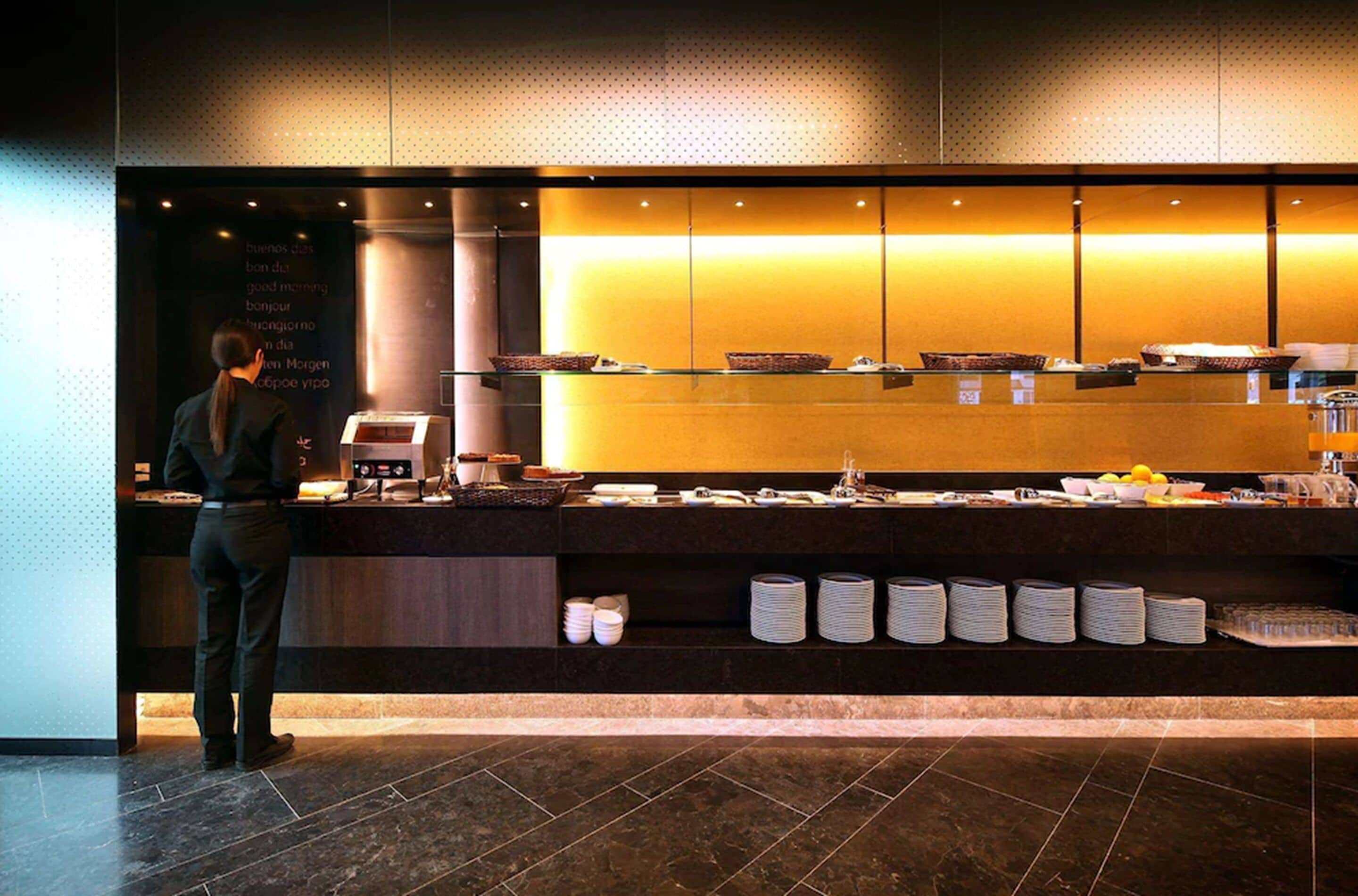 A hotel reception area with a counter, a staff member, and a variety of amenities including baskets, plates, and a coffee machine.