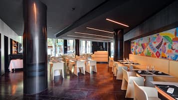 A modern restaurant with a central column, white tables, and a colorful mural on the wall.