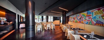 A modern restaurant with a central column, white tables, and a colorful mural on the wall.