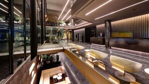 A modern hotel lobby with a central seating area, a reception desk, and a staircase leading to upper floors.