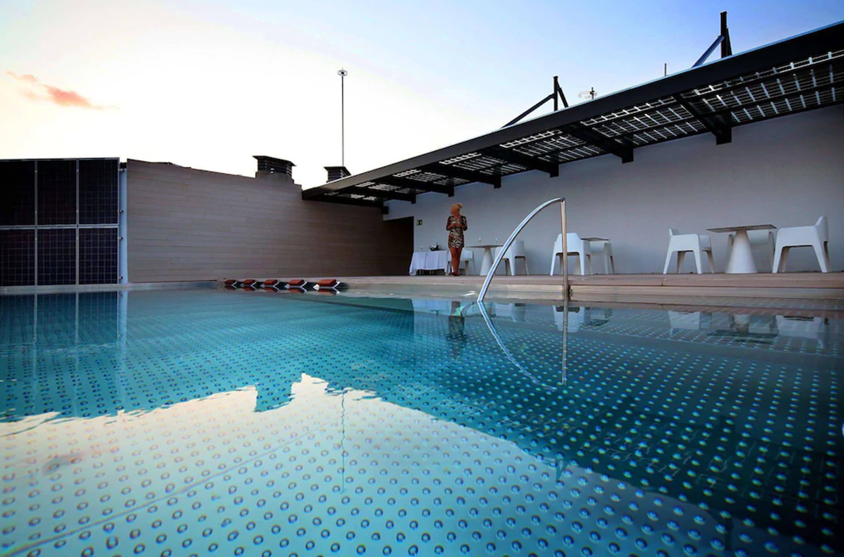 An indoor swimming pool with clear blue water, white lounge chairs, and a covered seating area.