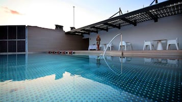 Une piscine intérieure à l’eau d’un bleu cristallin, dotée de chaises longues blanches et d’un espace détente abrité.