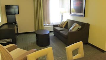 Une chambre d’hôtel avec un canapé, des fauteuils, une télévision, une lampe et un tableau encadré au mur.