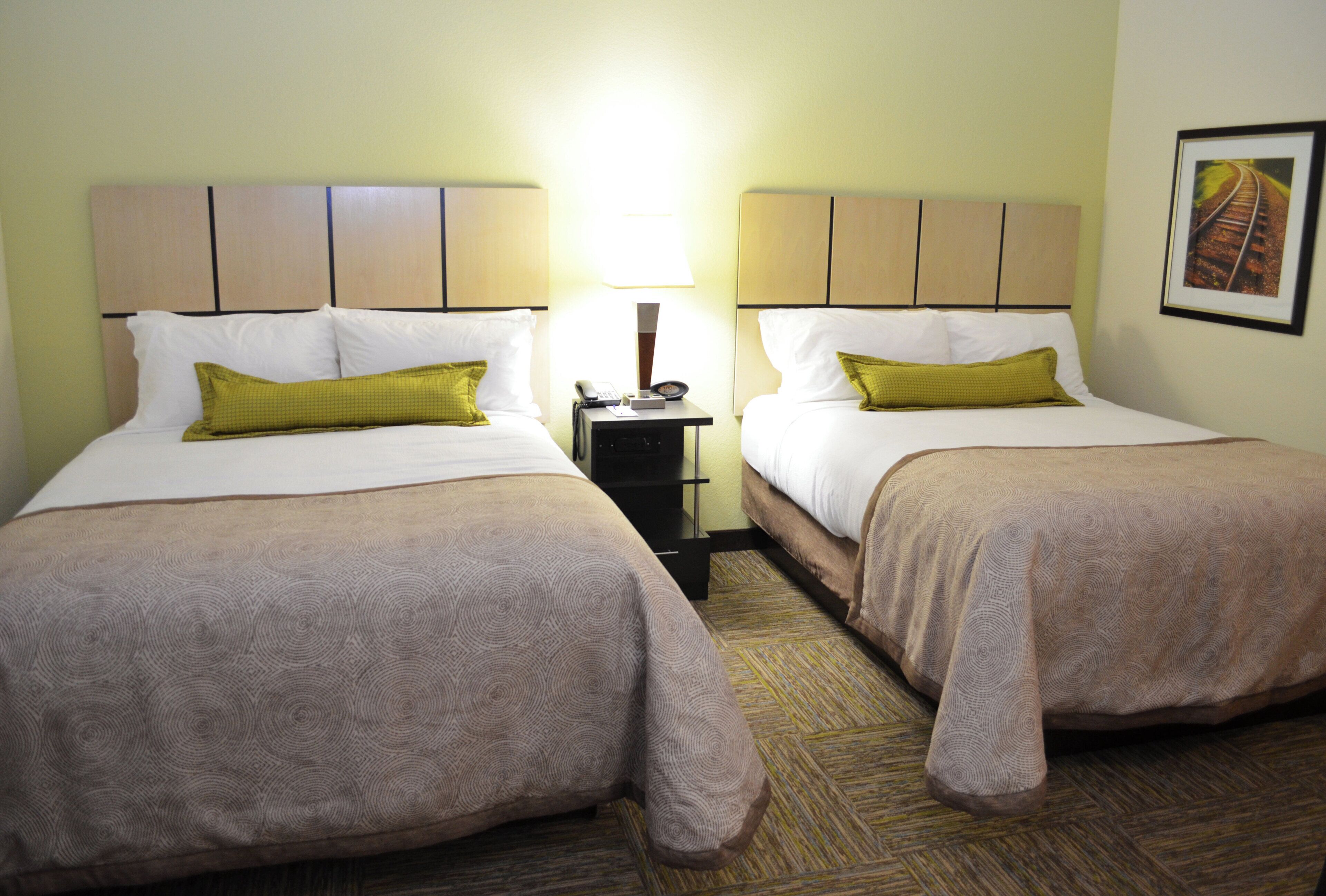 A hotel room with two beds, a nightstand, a lamp, and a framed picture on the wall.