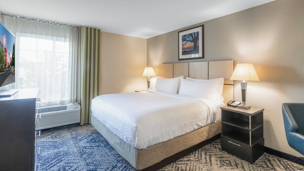 A hotel room with a large bed, two bedside lamps, a desk with a telephone, and a chair. - Candlewood Suites Greenville by IHG (Greenville)