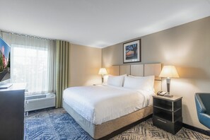 Quarto de hotel com uma cama grande, duas luminárias de cabeceira, uma mesa com telefone e uma cadeira.