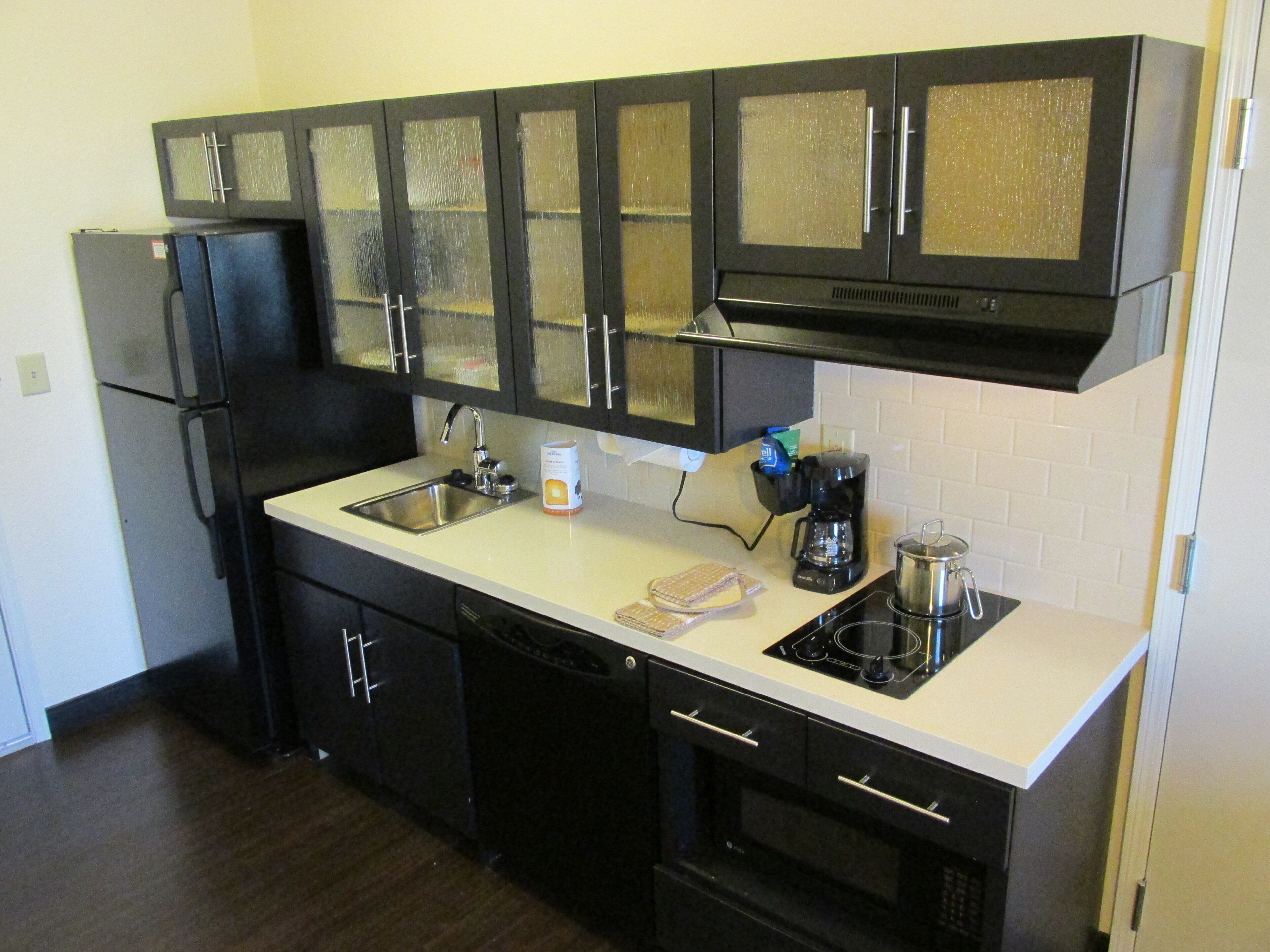 A kitchen with black cabinets, a stainless steel sink, a coffee maker, and a stove.
