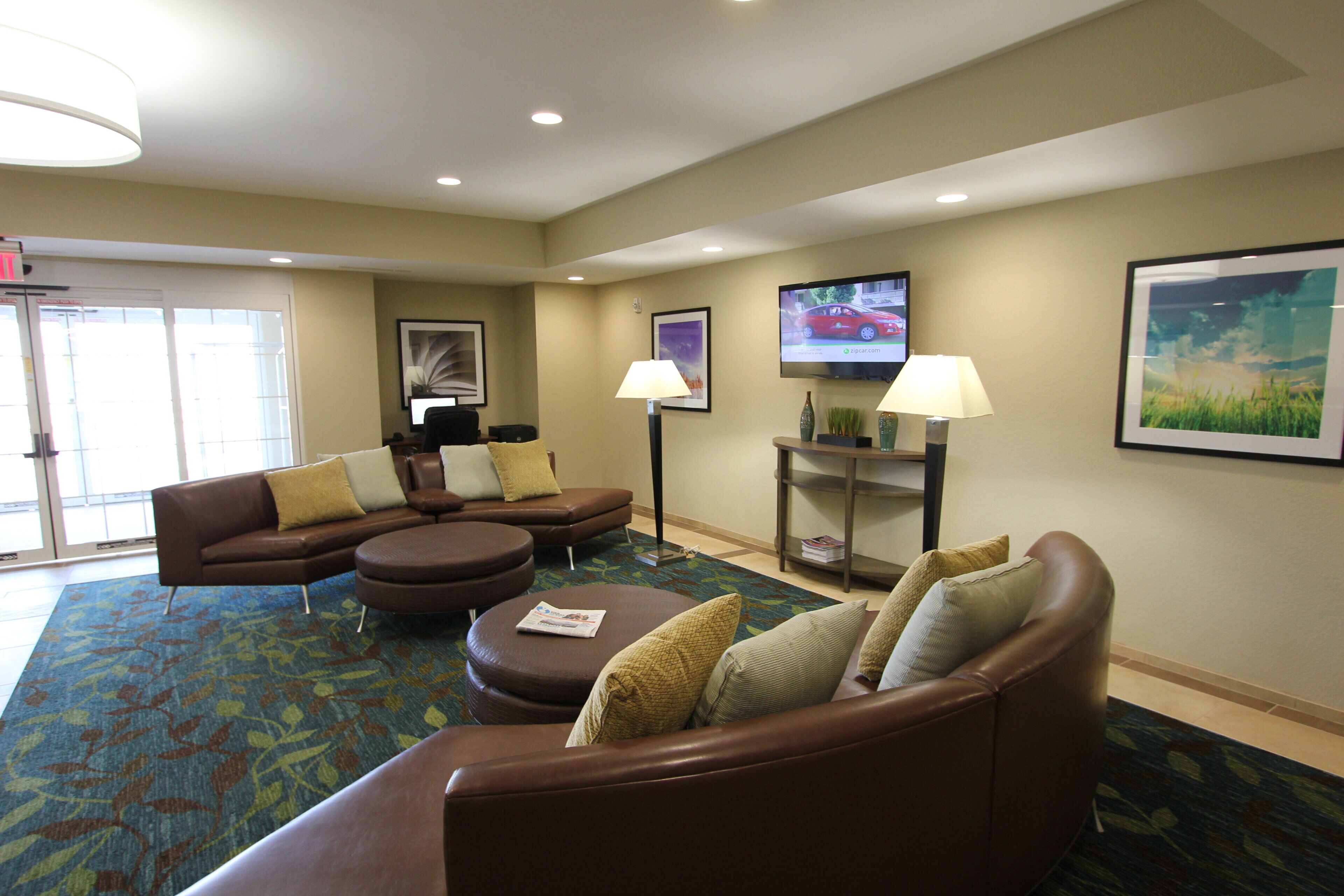 A hotel lobby with a brown leather sofa, a coffee table, and a television on the wall.