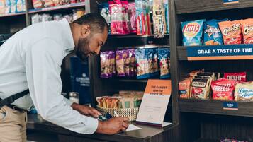 A person at a checkout counter in a store, with various snack items on shelves behind them.