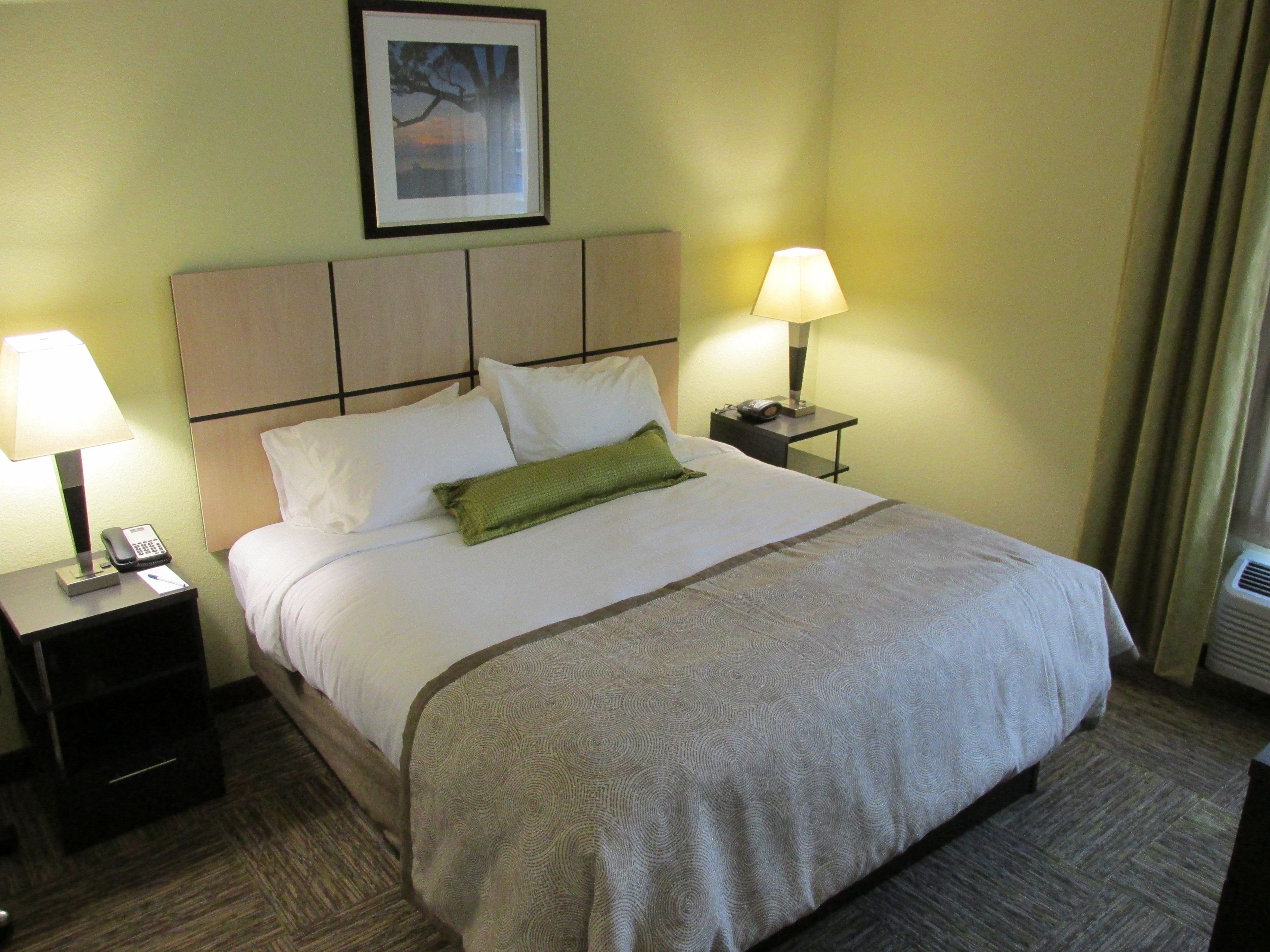 A neatly made bed with a patterned bedspread, two bedside lamps, a framed picture on the wall, and a small nightstand with a phone.