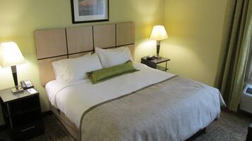 A neatly made bed with a patterned bedspread, two bedside lamps, a framed picture on the wall, and a small nightstand with a phone.
