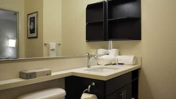 Een badkamer met een wit wastafel, een spiegel, een toilet en een zwart kastje met planken.