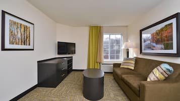 A hotel room with a flat-screen TV, a sofa, a desk with drawers, a trash bin, and two framed pictures on the walls.