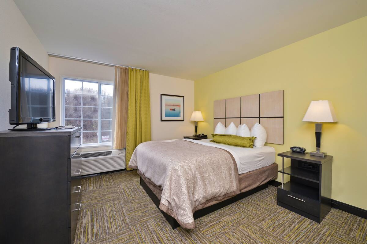 Ein Hotelzimmer mit Bett, Schreibtisch, Fernseher, Fenster und Lampe.