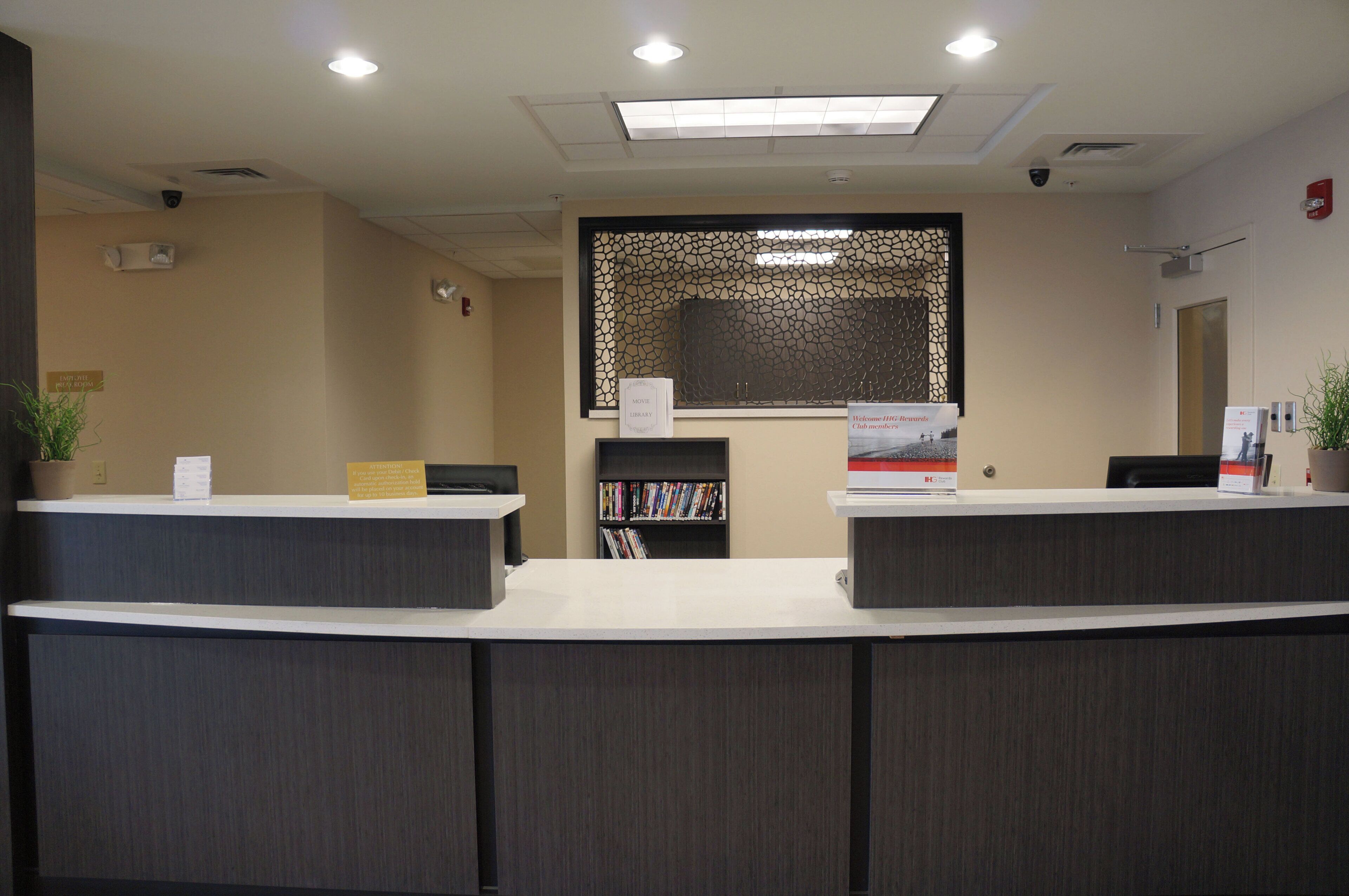 A reception desk area with a check-in counter, a waiting area with a sofa, a bookshelf, and a decorative wall panel.