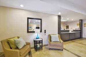 A hotel lobby with a reception desk, two armchairs, a lamp, and a mirror on the wall. - Candlewood Suites Harrisburg - Hershey by IHG (Harrisburg)