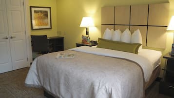 A hotel room with a bed, two bedside lamps, a desk, a chair, a framed picture on the wall, and a door.
