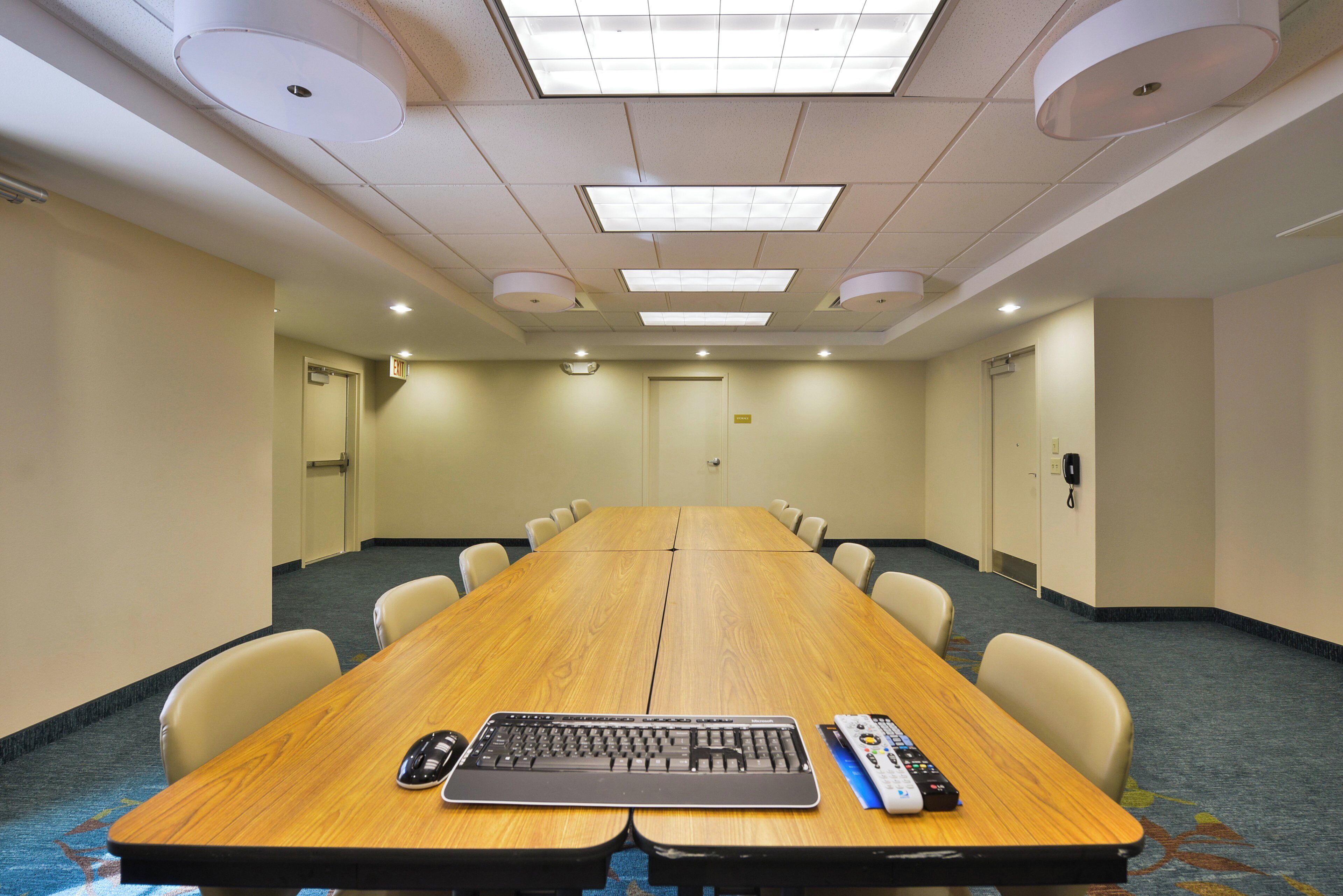 Une salle de conférence avec une longue table, des chaises, un clavier et une télécommande.