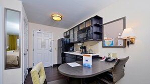 Habitación de hotel compacta con kitchenette, una zona de comedor con mesa y sillas, un espejo y una lámpara.