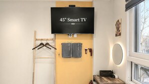 Habitación con un televisor Smart de 45 pulgadas montado en la pared, una escalera de madera, dos toallas, un extintor, una mesa de madera y una ventana con vistas.