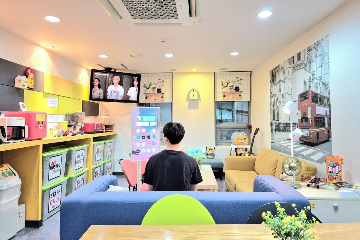 A hotel room with a sofa, a TV, a desk with a computer, and a wall with a cityscape mural.