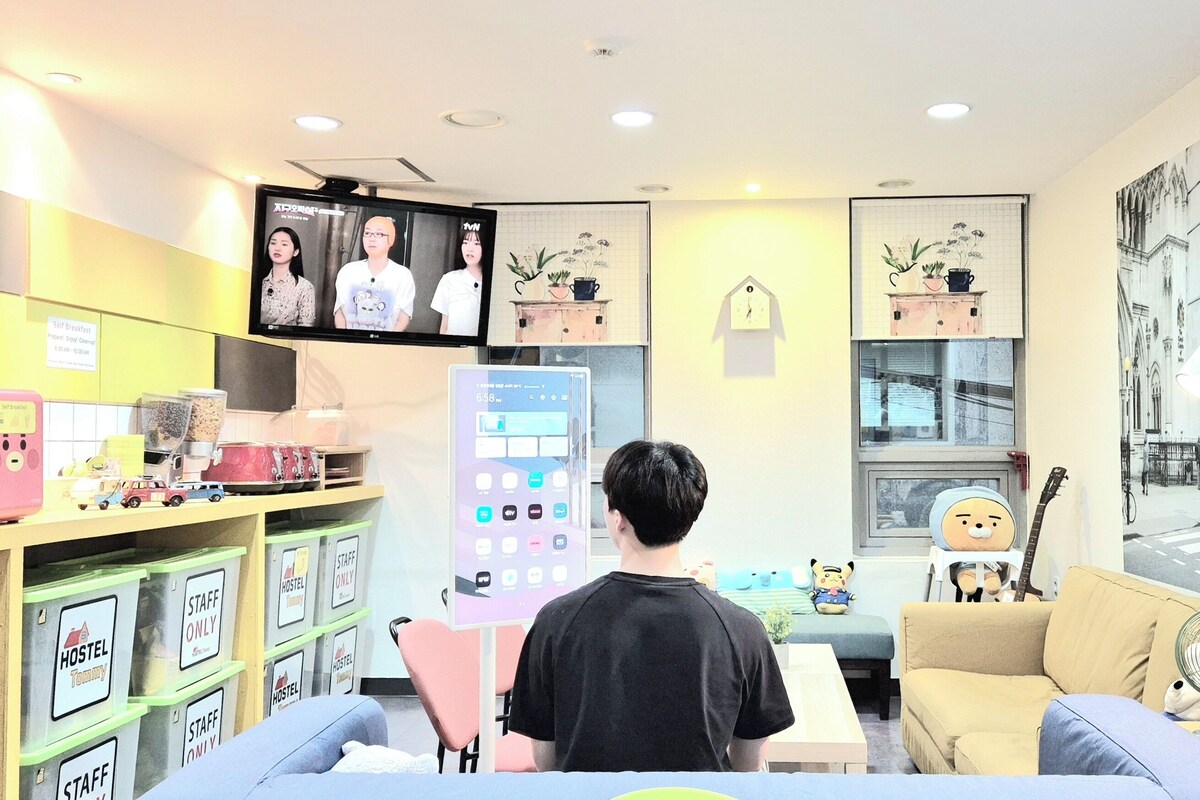 A room with a TV, a digital clock, a sofa, a table, and a wall clock.