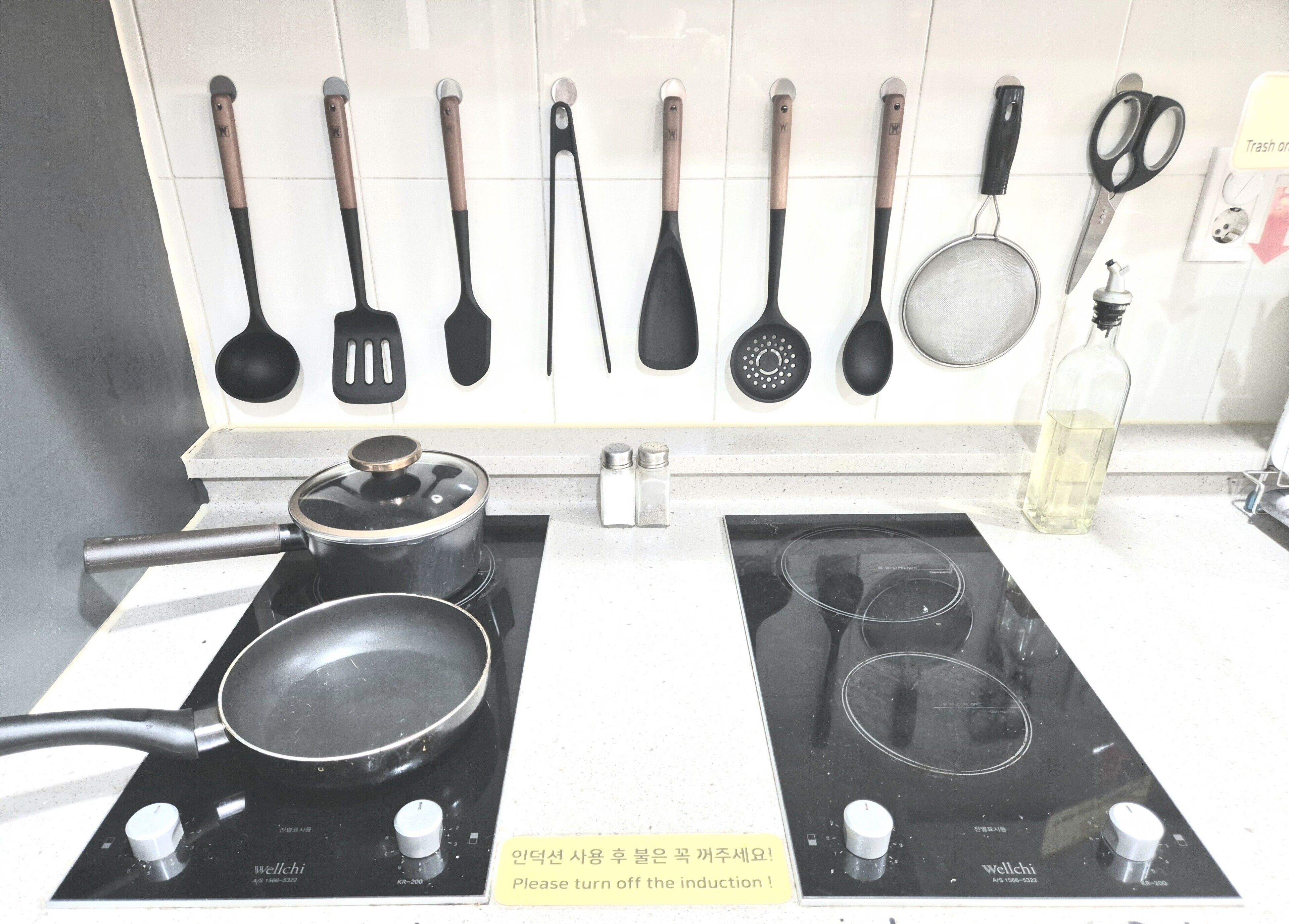 A kitchen with two induction cooktops, a range hood, and various utensils hanging on the wall.